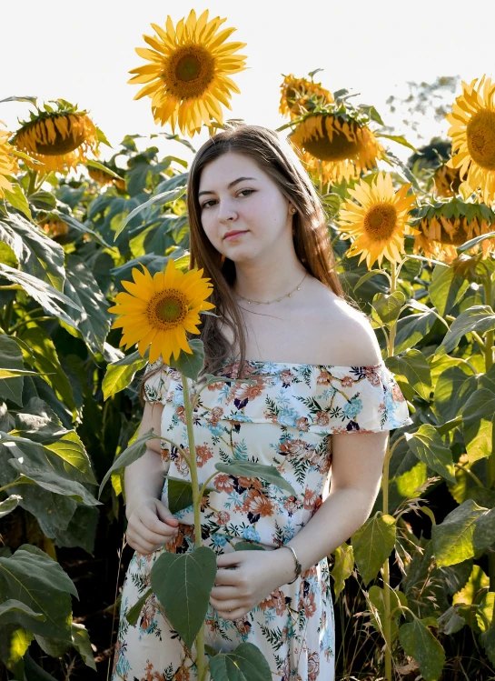 a woman in a dress holding sunflowers outside