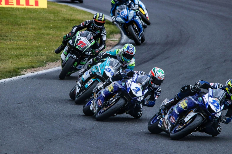 five motorcycle racers riding different bikes on a track