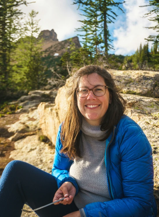 woman in a jacket sitting on rocks with pine trees