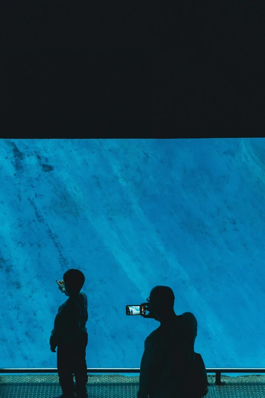 two people take a picture of a blue aquarium