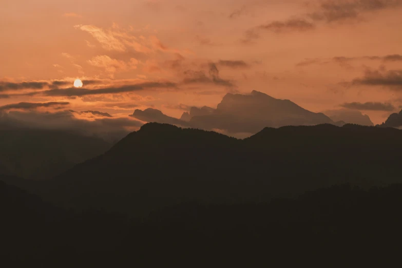 a sunset in a mountain range with a plane in the sky