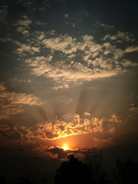 the sun setting behind clouds and trees