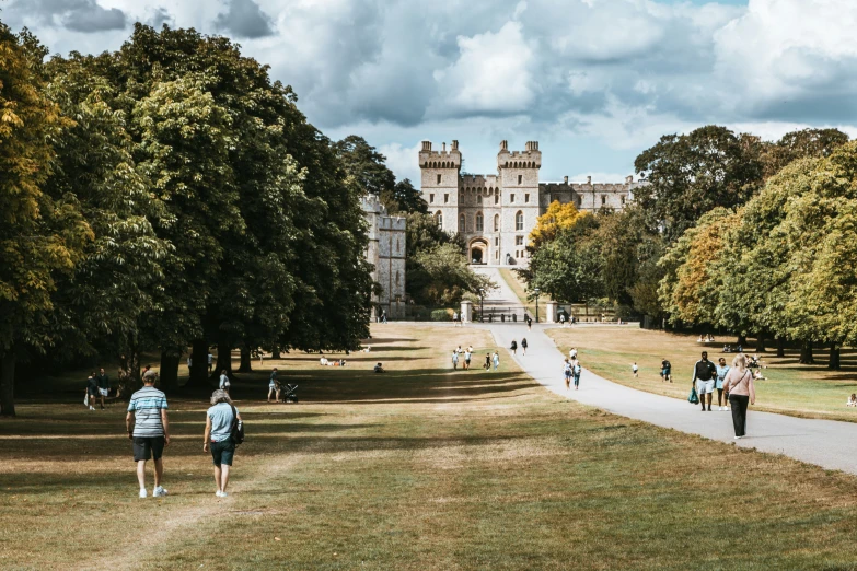 people are walking through a park near some very big houses