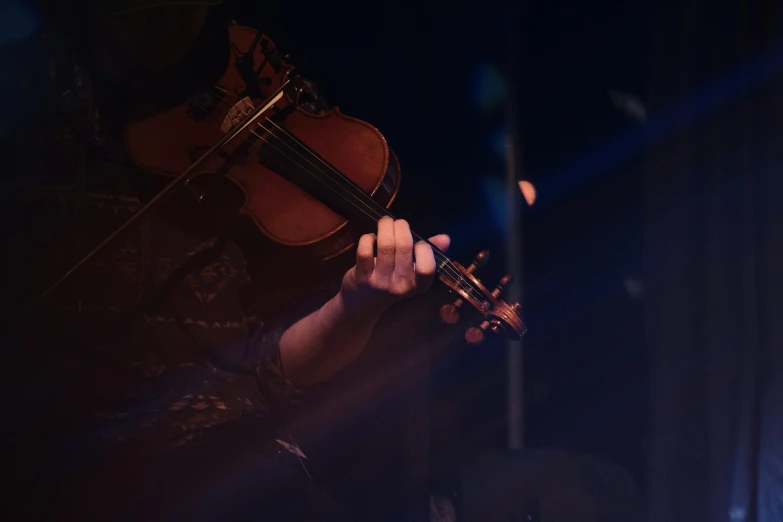 a man playing a violin on stage with lights shining behind him