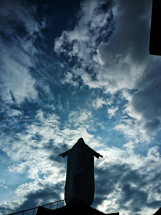 a tall, slender statue stands in the midst of some cloudy skies