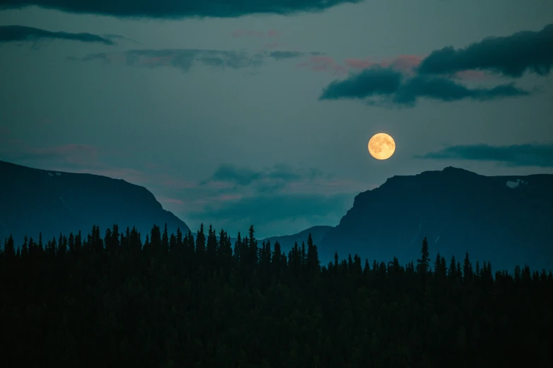 the moon is setting in front of some mountains