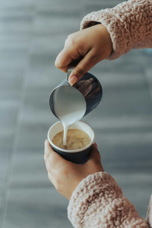 a person pours milk from a paper cup into a coffee cup