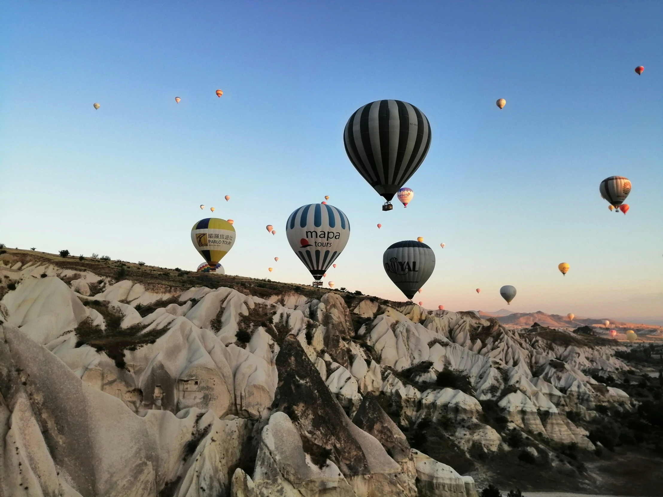 a group of  air balloons flying over the rocks