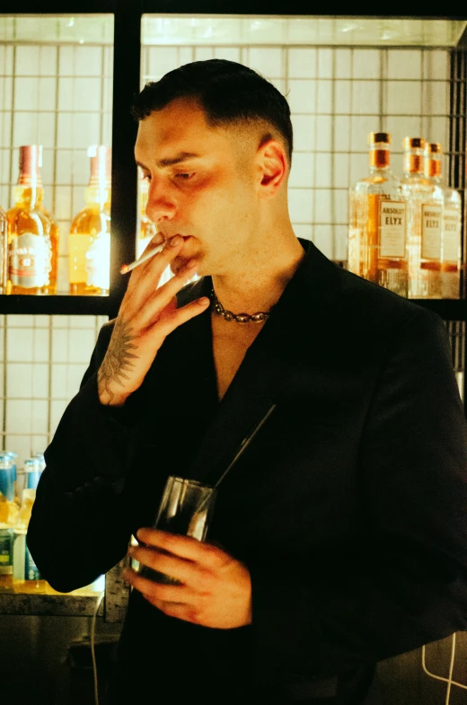 a man smokes a cigarette while standing in front of shelves with liquor bottles