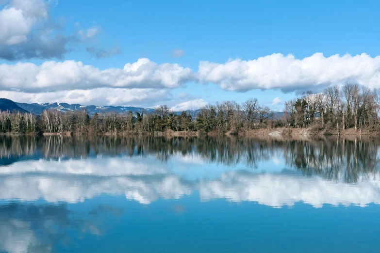 a lake surrounded by trees and mountains under a blue cloudy sky