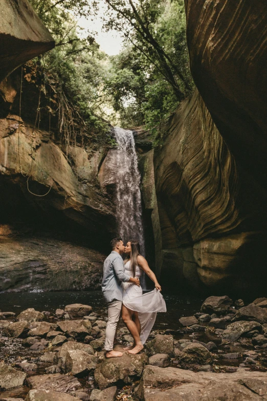 couple posing under waterfall, surrounded by stone pavement