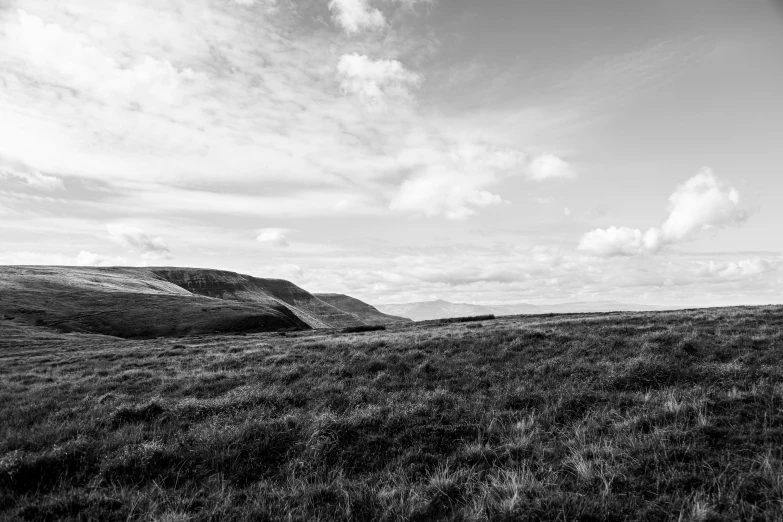 a lone hill with grass in the foreground and clouds in the distance