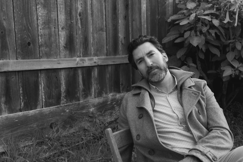 a man sitting on top of a bench next to a wooden fence