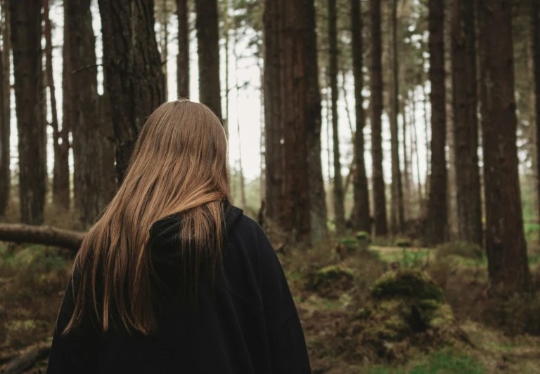 a woman standing in the middle of a forest looking at a fallen tree