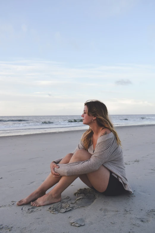 a young woman is sitting on the beach near the ocean