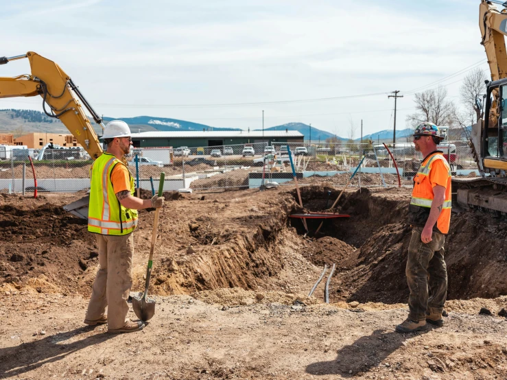 two construction workers stand at an area of dirt