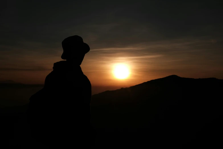 a person wearing a hoodie standing in front of a sunset