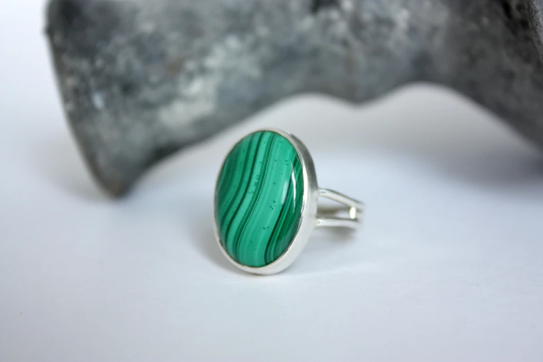 a green oval shaped ring is sitting on a rock