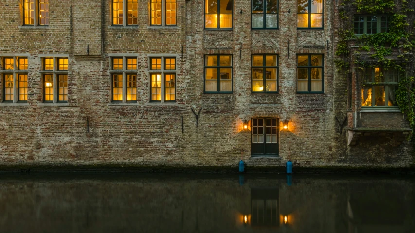 a tall brick building with two windows sitting on the side of a lake