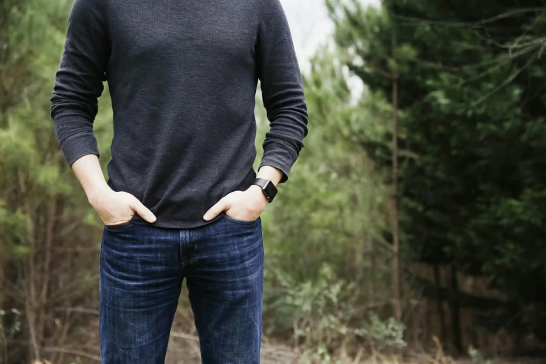 a man standing in a forest with his hands behind his waist