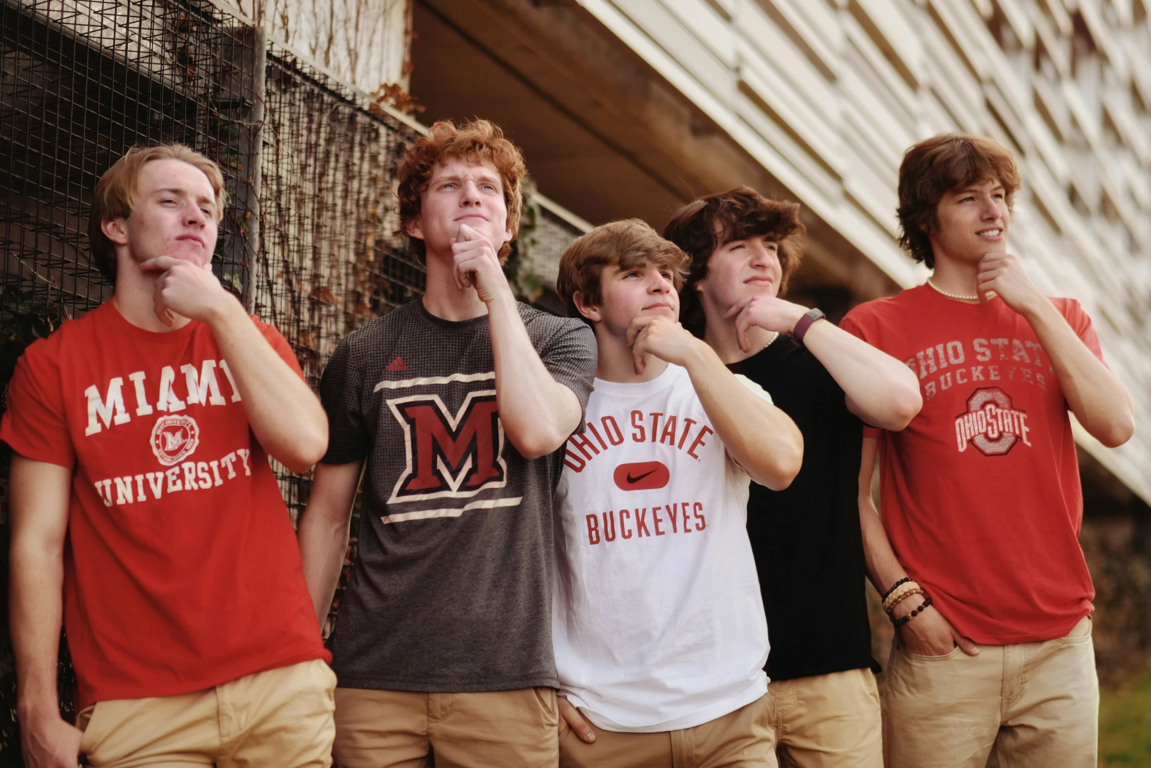 five male youth stand against a chain link fence