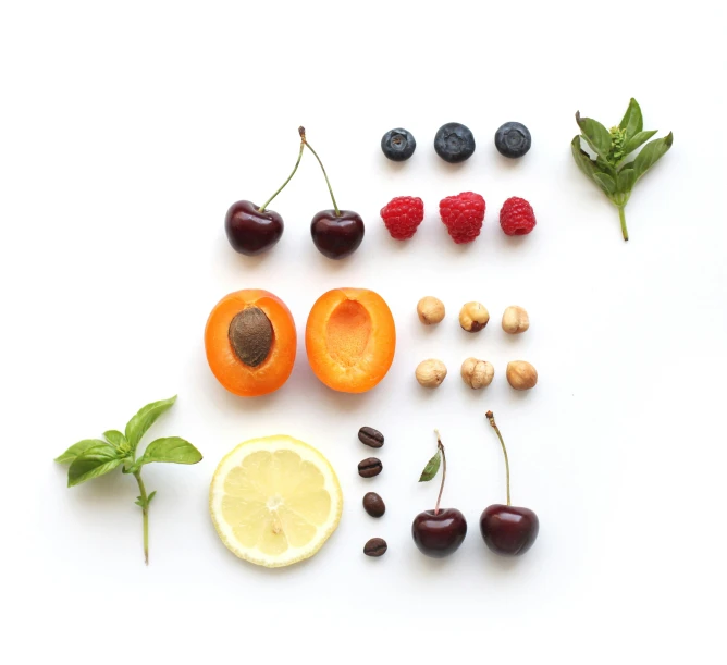 a white table with assorted fruits and vegetables, including nuts, fruit, mint, blueberries, and cherries