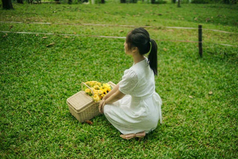 a woman sitting on the ground in the grass holding a basket with flowers