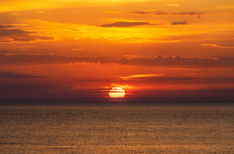 the sun is setting over the ocean and people are on a beach