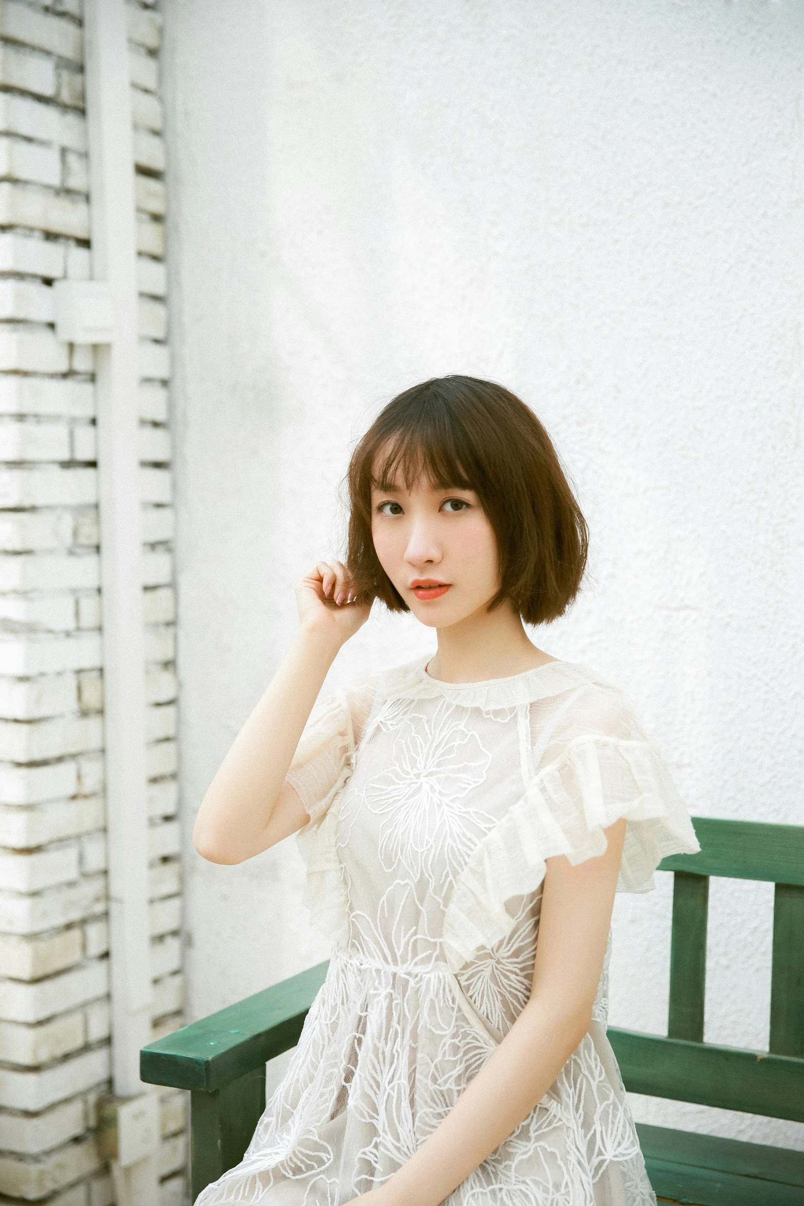 a woman wearing a white dress sitting on a green bench