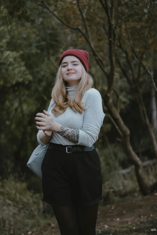 a girl in a red hat and sweater is standing near some trees