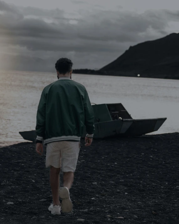 man walking on beach near boat with cloudy sky