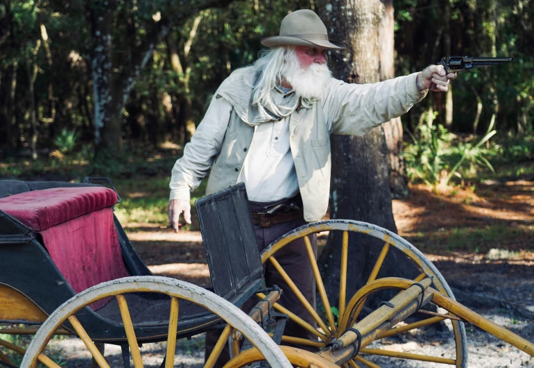 an old man with a gun on the back of a carriage