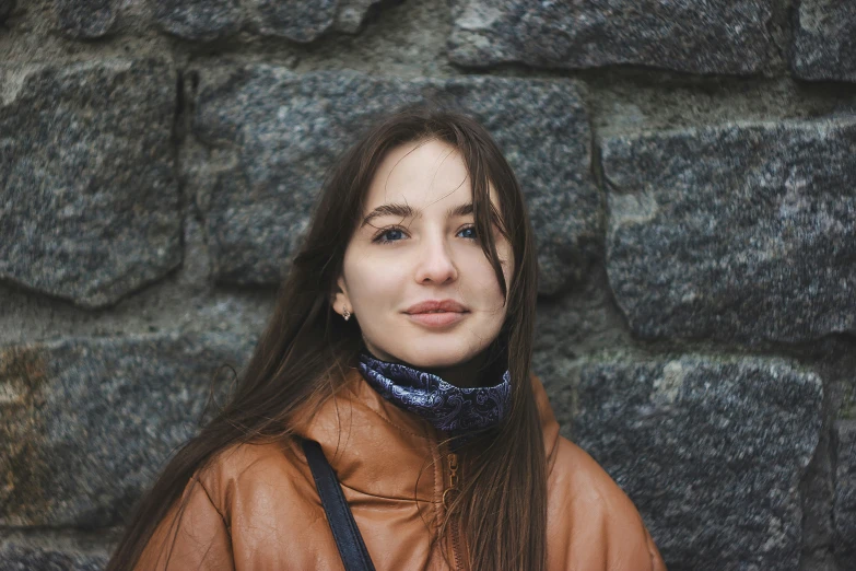 the young woman is standing near a stone wall