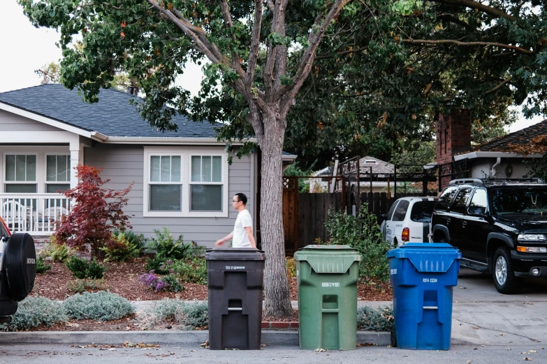 a person walking by two trash cans and a tree