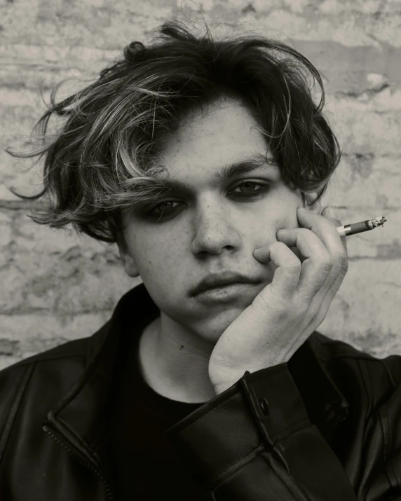 young man in black leather jacket holding cigarette to face