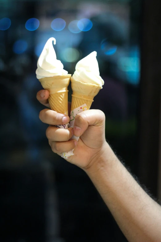 a person's hand holding two ice cream cones