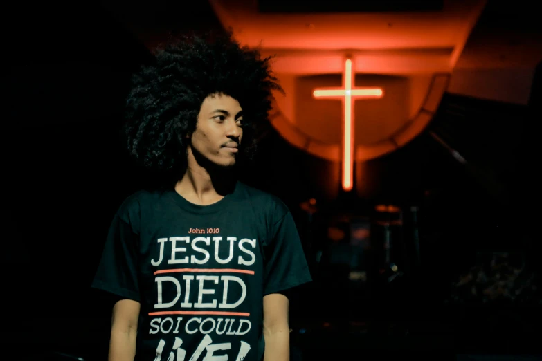 a man with curly hair posing in front of a cross