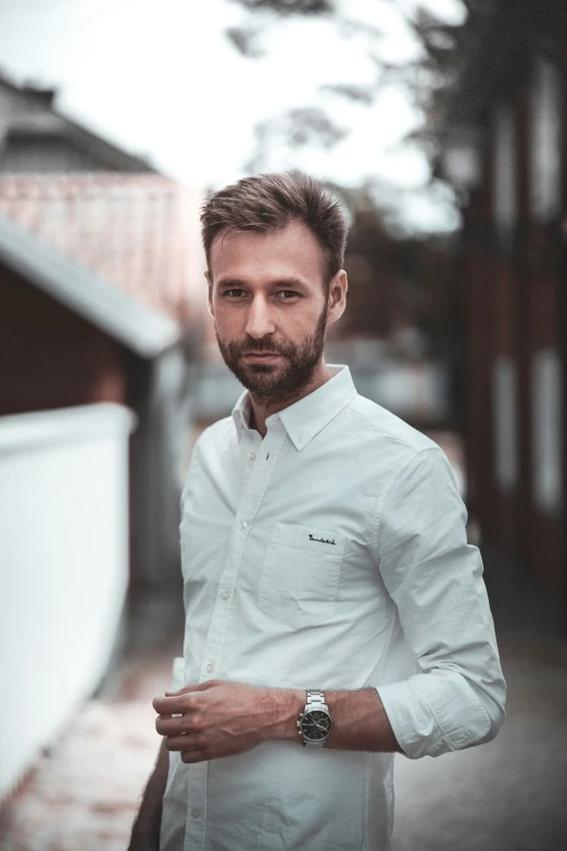 a bearded man standing on a sidewalk in a white shirt