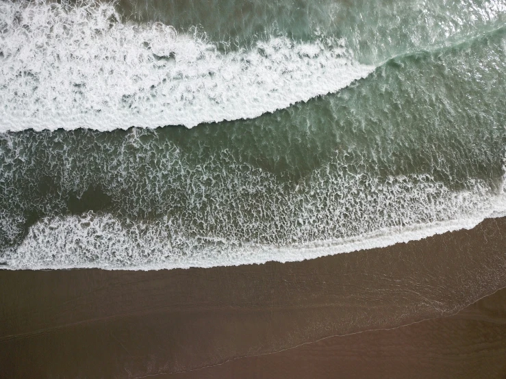 aerial view of surf with sandy beach on bottom and ocean in background