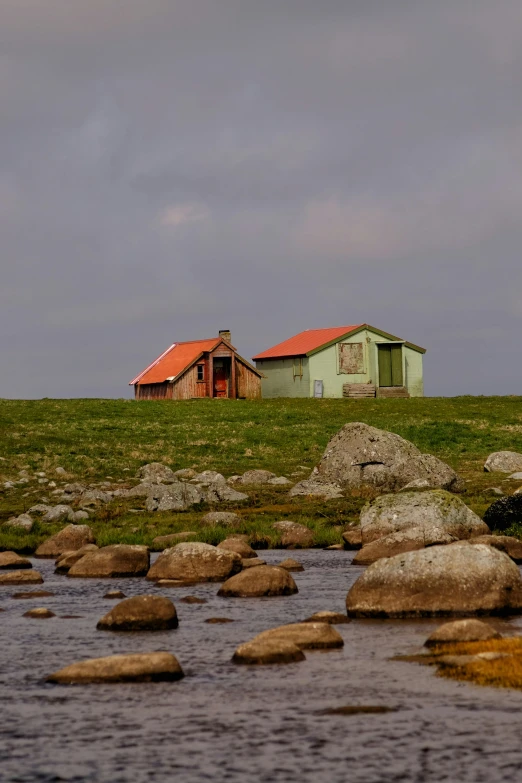 an old barn with a red roof sits in the middle of a grassy field next to a body of water