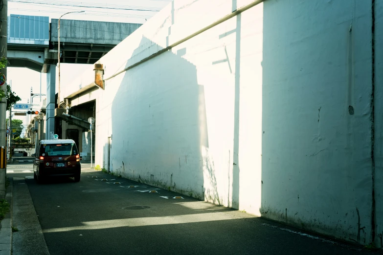 a car parked on a street in front of a wall and underneath a bridge