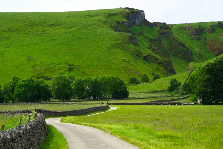 a scenic green pasture with a stone wall and road leading up the hill