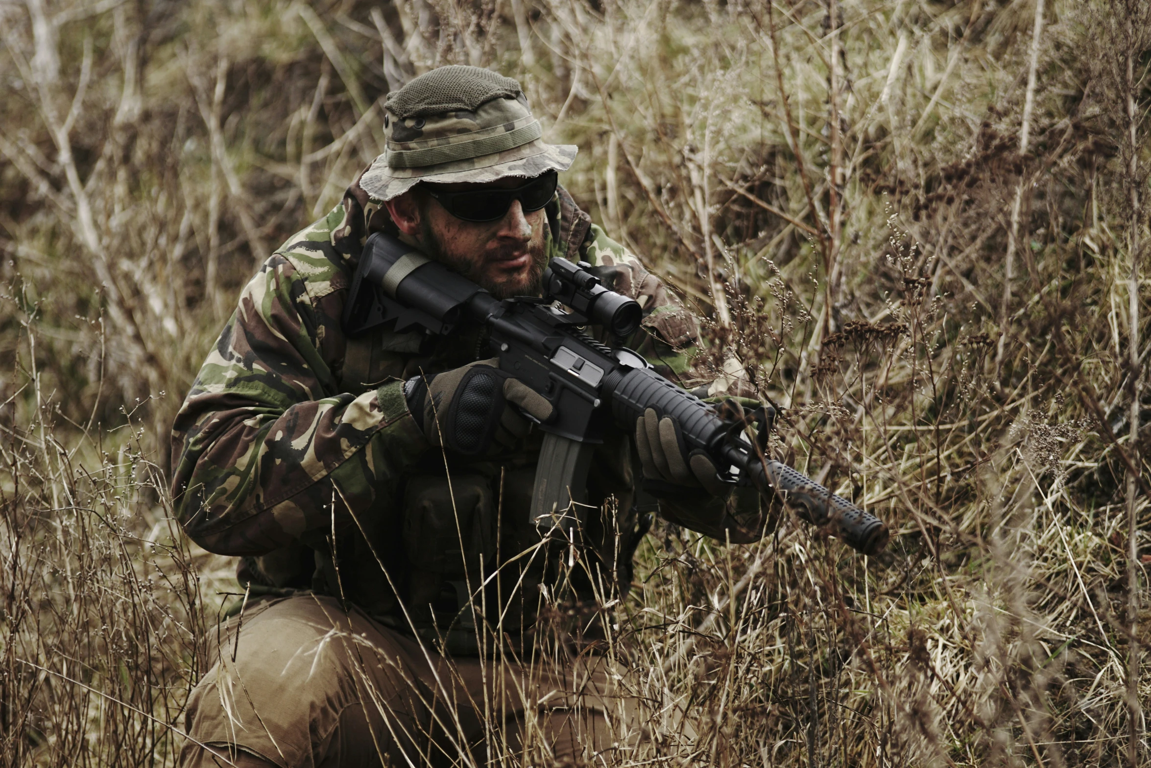 man with rifle in grassy area with weeds