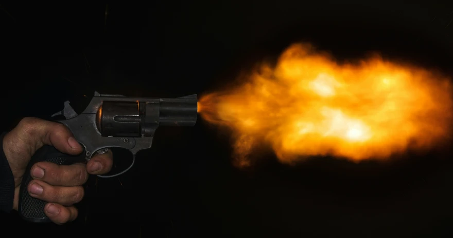 the man is holding a revolver while it is on fire