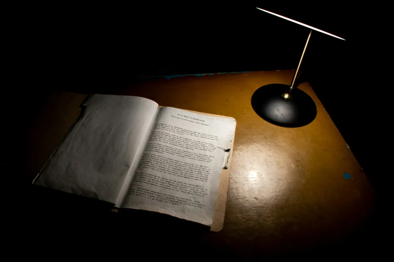 an open book and lamp on a desk in the dark