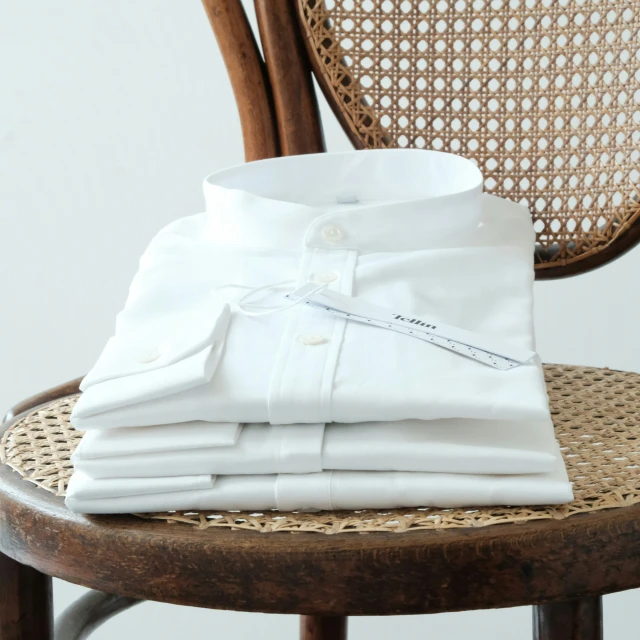 a stack of folded white shirts sits on top of a wooden chair