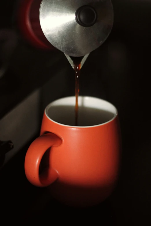 a metal coffee pot pouring coffee into a red cup