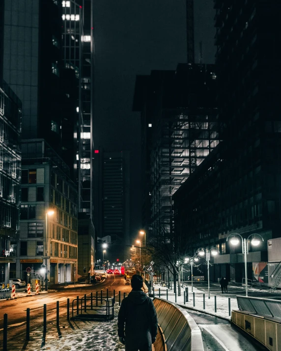 man walking down sidewalk near fence in large city at night