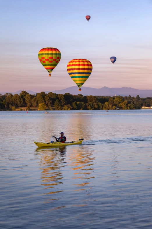 three  air balloons floating above water with a person in a canoe