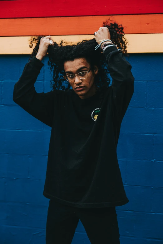 a man with curly hair standing in front of a blue wall